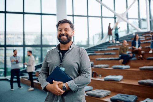 Happy businessman attending an education event at convention center and looking at camera. Happy business seminar presenter at conference hall looking at camera. Copy space.